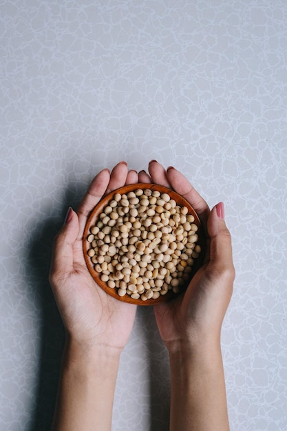 Hands serving soybean seeds in wooden bowl isolated on gray background.