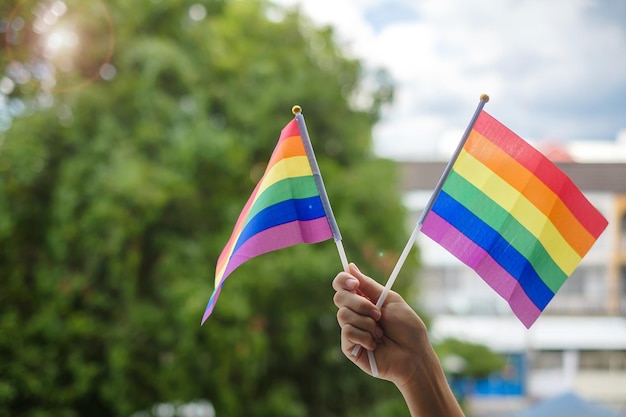 Hands showing LGBTQ Rainbow flag on green nature background Support Lesbian Gay Bisexual Transgender and Queer community and Pride month concept