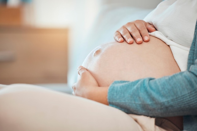 Hands stomach and pregnant with a woman sitting in the bedroom of her home alone while touching her belly Mother love and baby with a female parent holding her tummy while on the bed to relax