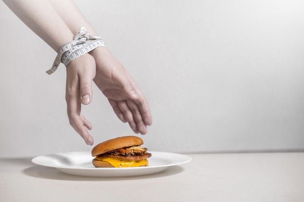 Hands take a burger,  centimeter ties hands, violation of diet,  hands reaching for a burger which lies on a plate on a white background