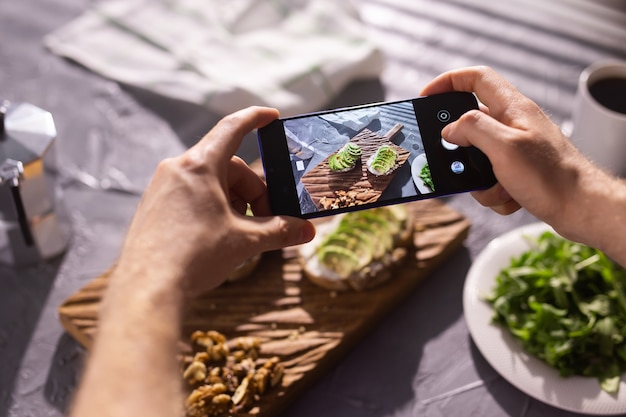 Hands take pictures on smartphone of two beautiful healthy sour cream and avocado sandwiches