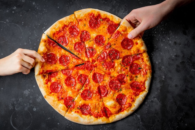 Hands take pieces of classic italian pizza pepperoni on black background, top view. High quality photo