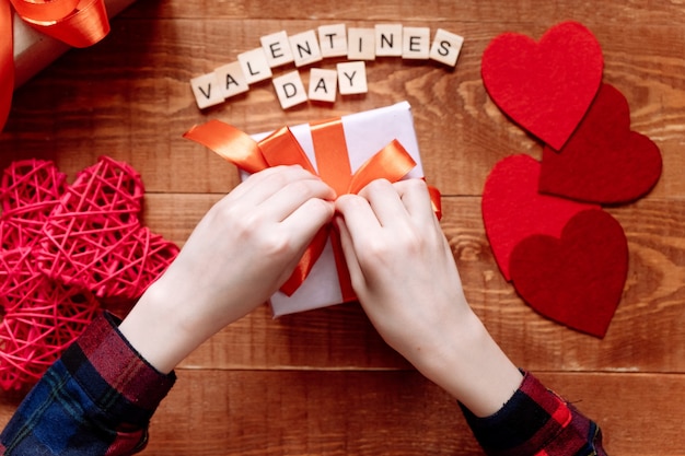 Hands of a teenager preparing a gift for Valentine's Day on a wooden background. Hearts and holiday decor on.