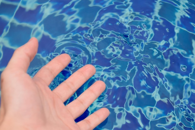 Hands touching the surface of the water until it forms waves with beautiful patterns closeup at outdoor swimming pool for concept of exercise and outdoor activities