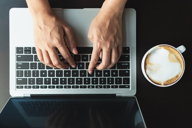 Hands typing a button on the laptop on a black wooden table 