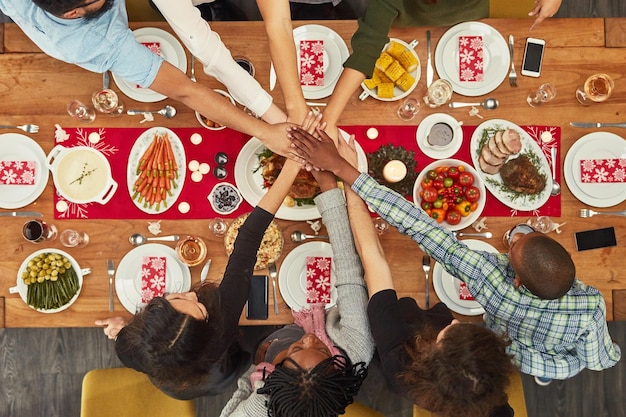 Hands unity and Christmas with a table setting for dinner or a celebration even with friends from above Food together and motivation with a group of people bonding during a meal in the holidays