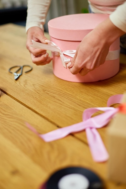 Hands of unrecognisable woman wrapping with ribbon a pink present