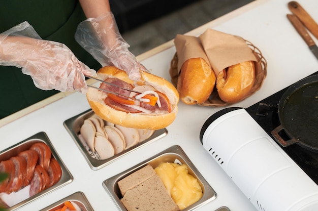 Hands of vendor putting meat and vegetables in cut bun, view from above