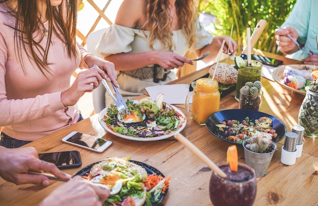 Hands view of young people eating brunch and drinking smoothies bowl with ecological straws in trendy bar restaurant. Healthy lifestyle, food trends concept