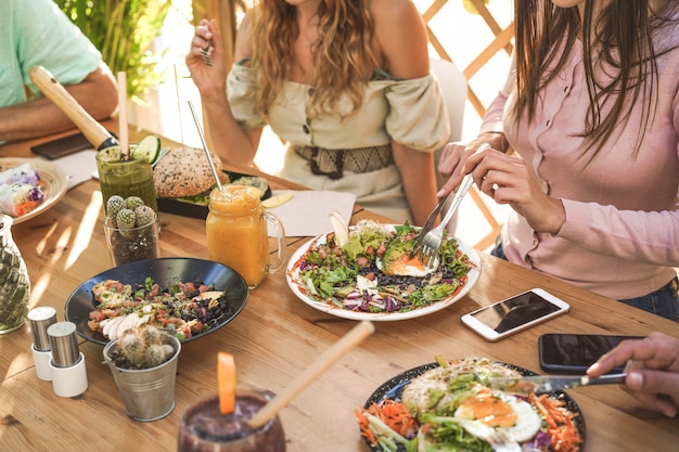 Hands view of young people eating brunch and drinking smoothies bowl with ecological straws in trendy bar restaurant