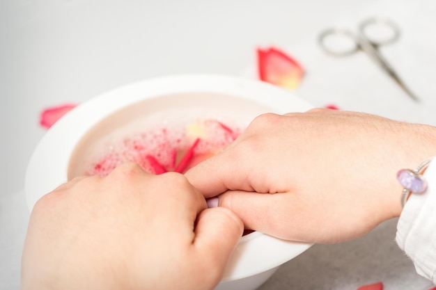 Hands in white bowl bathe nails with water and rose petals to soften the cuticle and dry skin.