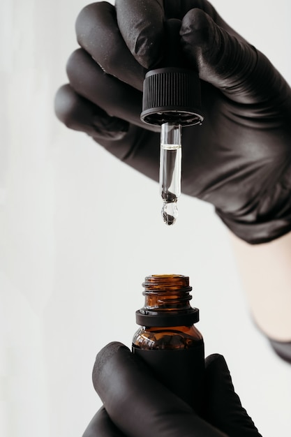 Hands with black gloves pouring oils from a cosmetic dropper bottle