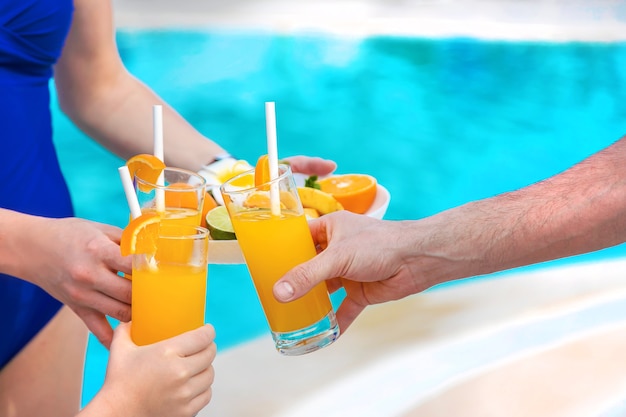 Hands with cocktails making a toast by the pool