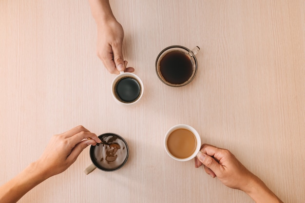 Hands with cups of coffee on wood surface