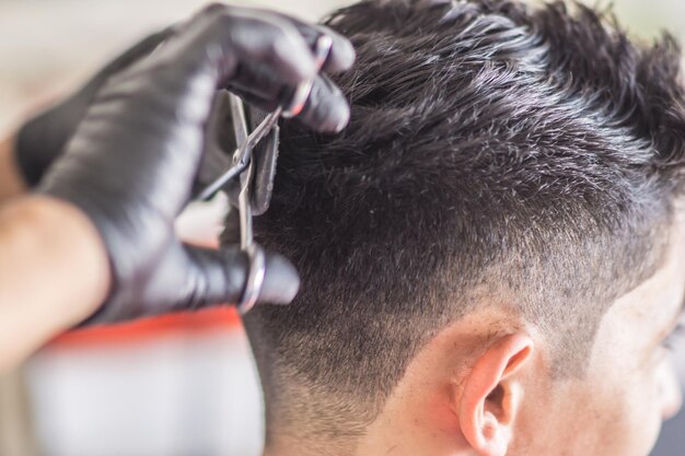 Hands with gloves of a barber cutting the hair of a latin costumer using scissors