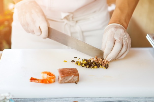 Hands with knife cutting olives. Piece of fish and shrimp. Tiny pieces of green olives. Restaurant employee cooking food.