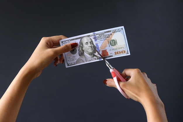 Hands with scissors cutting money. Scissors cutting one hundred dollar note.