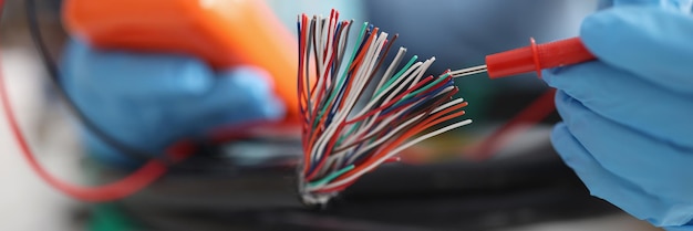 Hands with a voltmeter check colored wires in the cable blurry