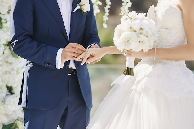 Hands with wedding rings. Modish groom putting a golden ring on the bride's finger during the wedding ceremony. Loving couple, a woman in a wedding dress and handsome man in a stylish blue suit