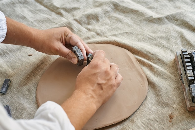 Hands of a woman artisan ceramist kneading a layer of clay on the table close-up