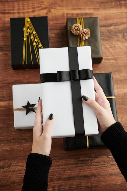 Hands of woman holding giftbox wrapped in white paper and decorated with black ribbon