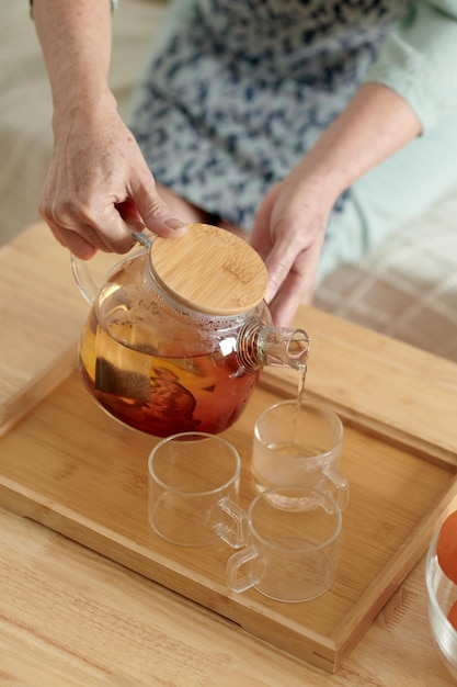 Hands of woman pouring black tea in cup on wooden tray