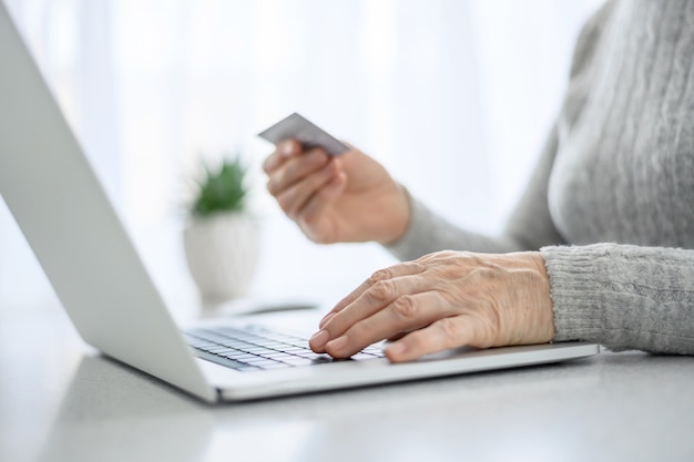 Hands of a woman senior work at a laptop with credit card using modern technology in everyday life. online shopping.