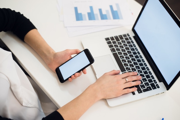 Hands of a woman using a phone and a laptop