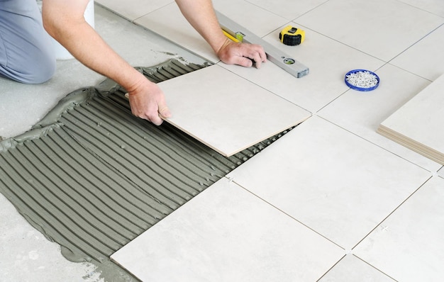 The hands of the worker are laying  the ceramic tile on the floor.