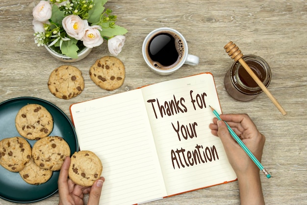 hands writing Thank you for your attention on notebook and eating homemade cookies