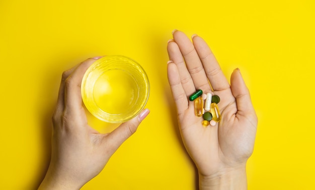 Hands on yellow surface, pills water cure virus. Selective focus