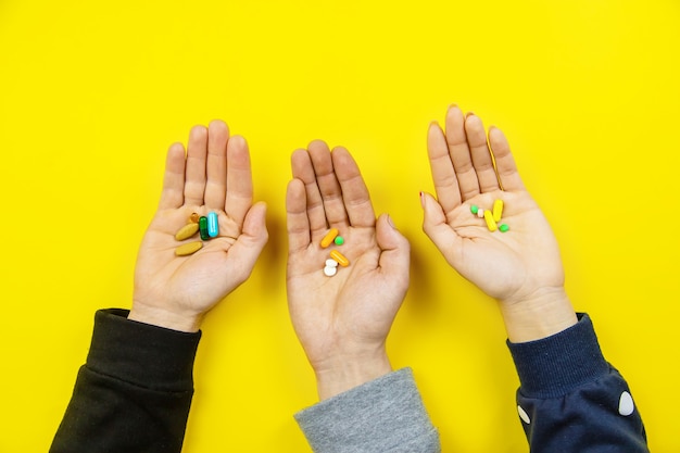 Hands on yellow surface, pills water cure virus. Selective focus