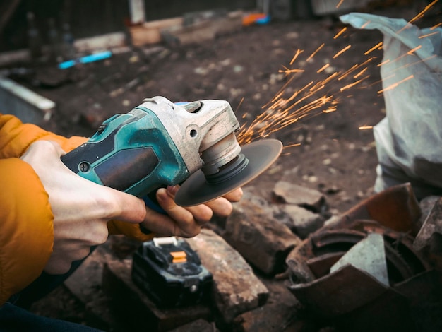 The hands of a young Caucasian man in a yellow jacket are holding a drill