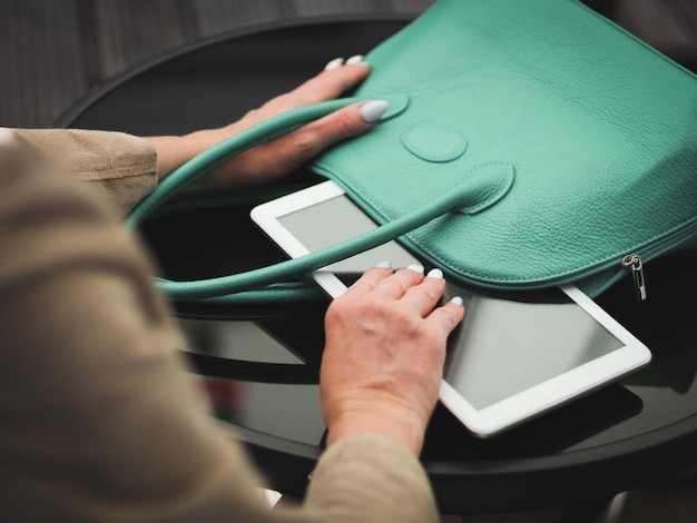 The hands of a young caucasian woman takes out her tablet from a green handbag