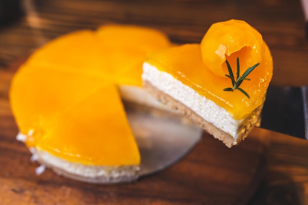 Hands of young chef baker cutting slice of mango cheesecake