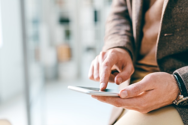 Hands of young elegant businessman pointing at smartphone screen or scrolling through information