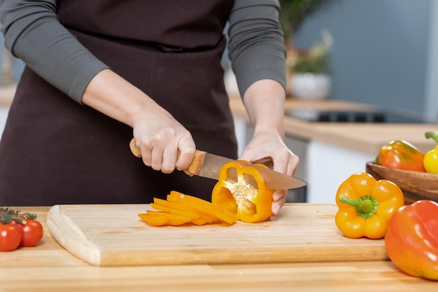 Hands of young female chopping fresh yellow capsicum