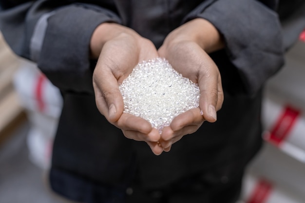 Photo hands of young female factory worker holding pile of unprocessed white plastic pellets in front of camera before processing raw materials