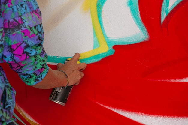 Hands of a young girl painting a graffiti on a wall with spray cans