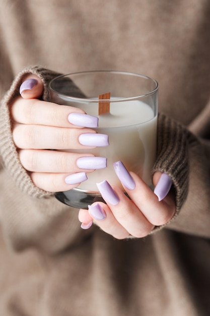 The hands of a young girl with a beautiful light purple manicure hold a candle