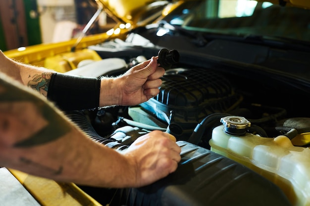 Hands of young man holding detail of car engine over open hood