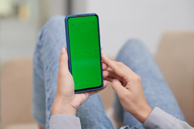 Hands of young modern woman holding mobile phone with blank green screen