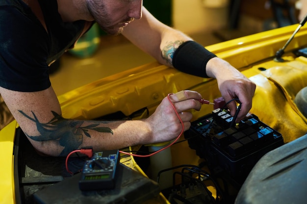 Hands of young technician bending over motor of car and using multimeter