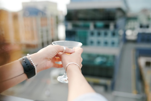 Hands of young woman holding martini glass with cocktail while having rest