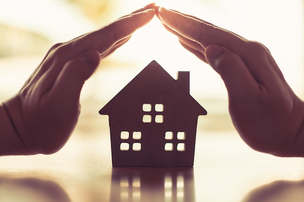 Hands of a young woman surround a wood house model. 