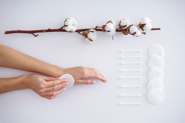 Photo hands of a young woman with a cotton branch, cotton pads and cotton buds on a white background. female manicure. cotton flower. spa concept. creative composition with cotton.