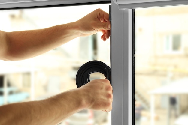 Hands of young worker applying rubber strip onto window in office