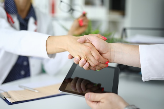 Handshake of two doctors one is holding tablet. Medical insurance agreements concept