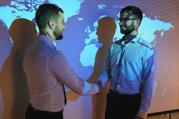 Handshake with map of the world in background two businessmen on the background of the world map shake hands the concept of international relations