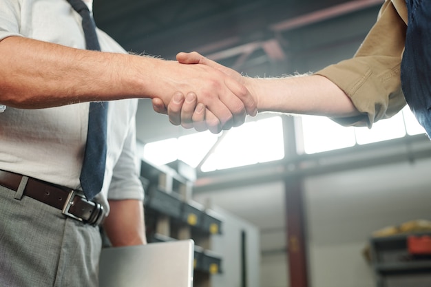 Handshake of young contemporary business partners or that of master and his trainee inside industrial plant